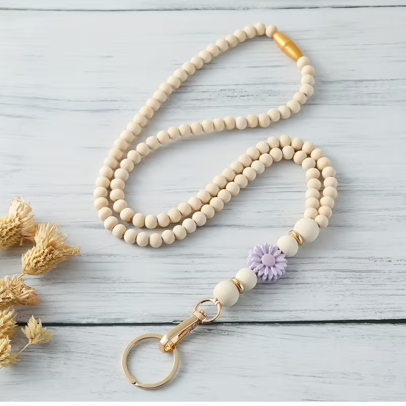 Handcrafted beaded lanyard featuring a soft lavender silicone daisy focal, natural beechwood beads, and gold accents with a safety breakaway clasp by Woodland Beads & Co.