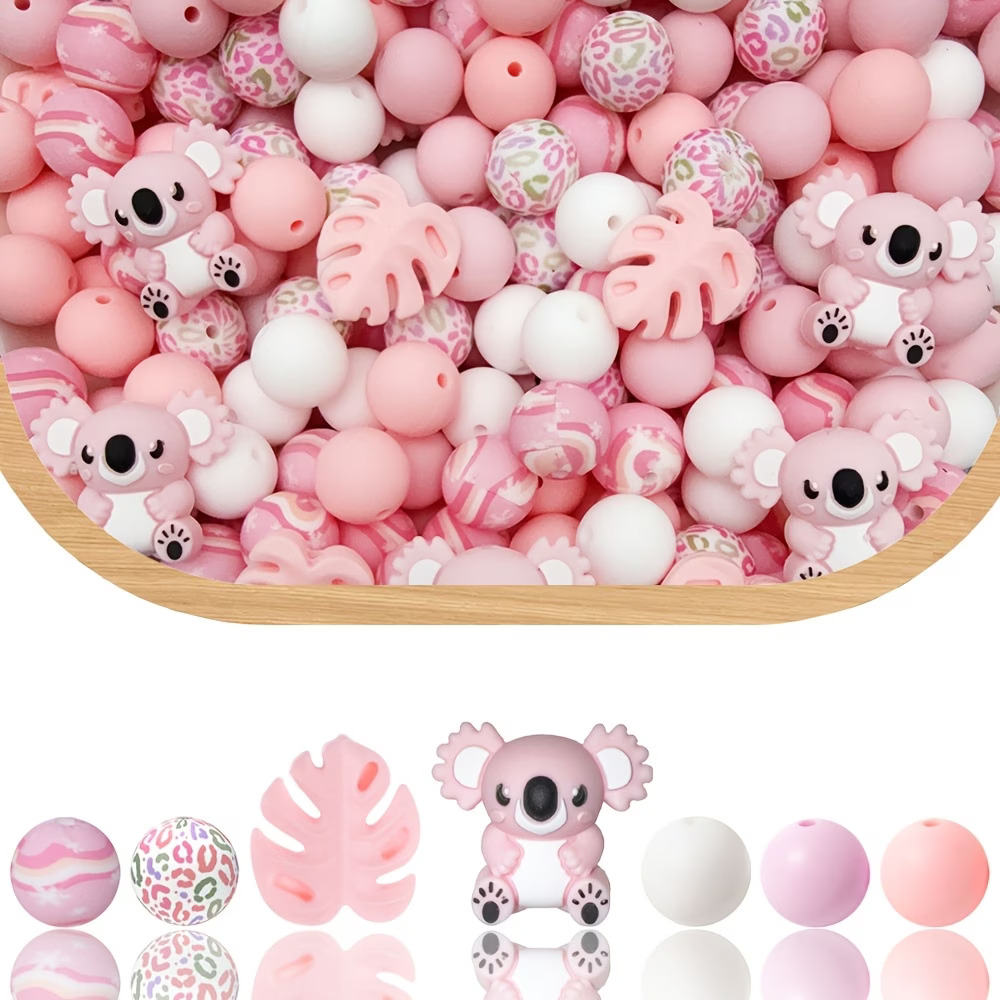 A product display from Pink Koala Leaf 44 Piece.jpg featuring a variety of pastel pink, peach, and white crafting beads. The upper portion shows a wooden bowl overflowing with a mixed pile of loose round and shaped silicone beads. Nestled within the pile are multiple small, pink cartoon koala focal beads and pink monstera leaf focal beads. The lower portion displays a clean, single row of the bead varieties with their reflections on a white surface below them, showcasing a pink marble-swirl bead, a multi-colored leopard print bead, a pink tropical leaf bead, a pink koala character bead, a solid white bead, a solid light pink bead, and a solid soft peach bead.