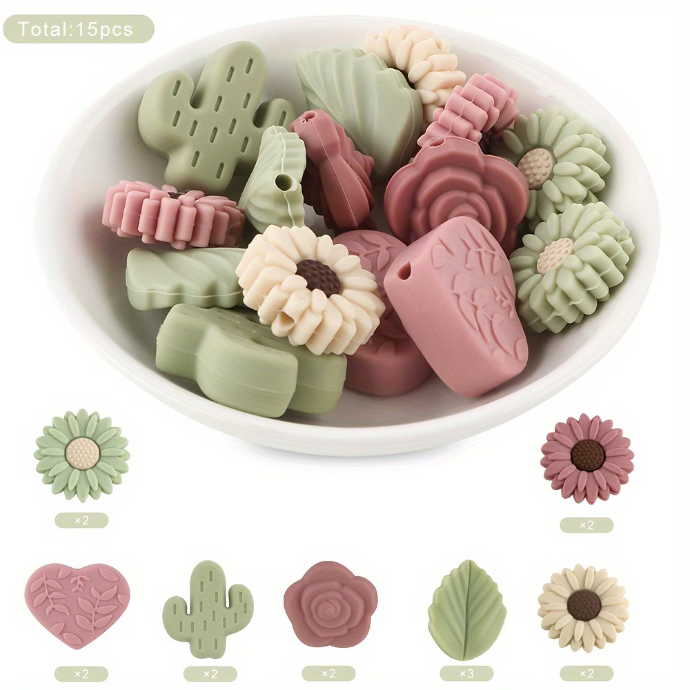 A white ceramic bowl filled with 15 decorative silicone focal beads in shapes of cacti, sunflowers, roses, and leaves in sage green, dusty rose, and cream colors.