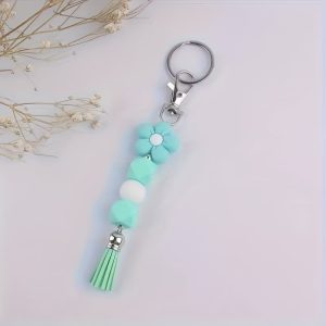 A decorative keychain featuring a lake blue cartoon flower silicone bead, geometric mint beads, a single white bead, and a matching mint tassel attached to a silver keyring.