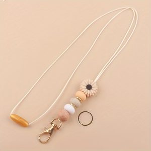 A beige lanyard keychain featuring a daisy silicone bead, a wooden bead, neutral silicone beads, and gold-tone hardware, displayed on a matching beige background.