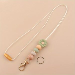 A pea green lanyard keychain featuring a daisy silicone bead, a wooden bead, earth-toned silicone beads, and gold-tone hardware, displayed on a neutral background.