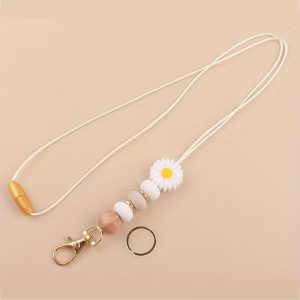 A white lanyard keychain featuring a daisy silicone bead, a wooden bead, neutral silicone beads, and gold-tone hardware, displayed on a neutral background.