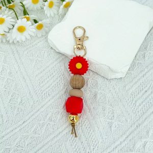 A handmade keychain featuring a red daisy silicone bead, a wooden bead, a neutral silicone bead, a red geometric bead, and a gold metallic bead, attached to a gold lobster clasp.