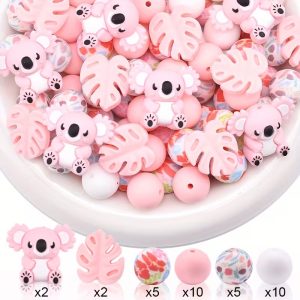 A product showcase for a 34-piece DIY silicone bead kit. The top half of the image shows a white bowl filled with a mix of light pink koala beads, pink monstera leaf beads, solid pink and white round beads, and floral-patterned round beads. The bottom half displays a clean row of the individual bead styles alongside their quantities: 2 pink koalas, 2 pink tropical leaves, 5 red floral round beads, 10 solid pink round beads, 5 multi-colored abstract floral round beads, and 10 solid white round beads.